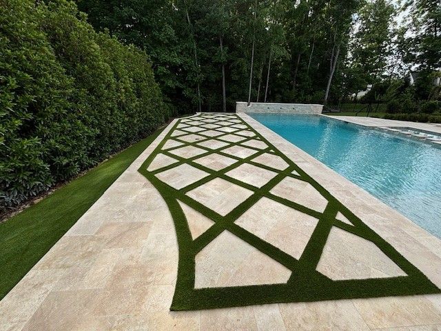 Geometric green turf pattern on a stone patio beside a swimming pool and hedge-lined garden