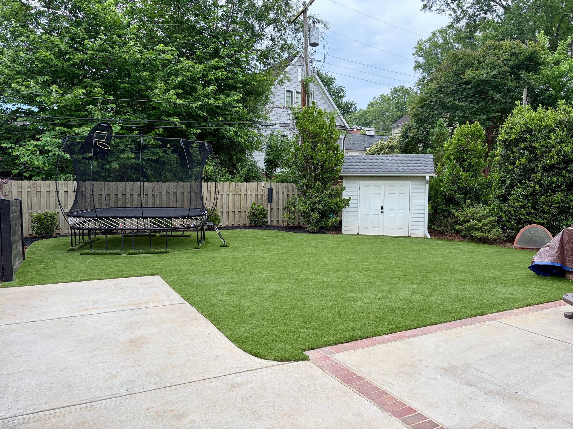 Backyard with green lawn, white shed, bench, and two concrete patios under trees