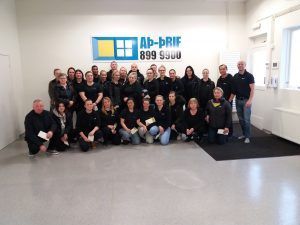 Hópur fólks situr fyrir inni í björtum skrifstofu með „AB-First“ skilti á veggnum.