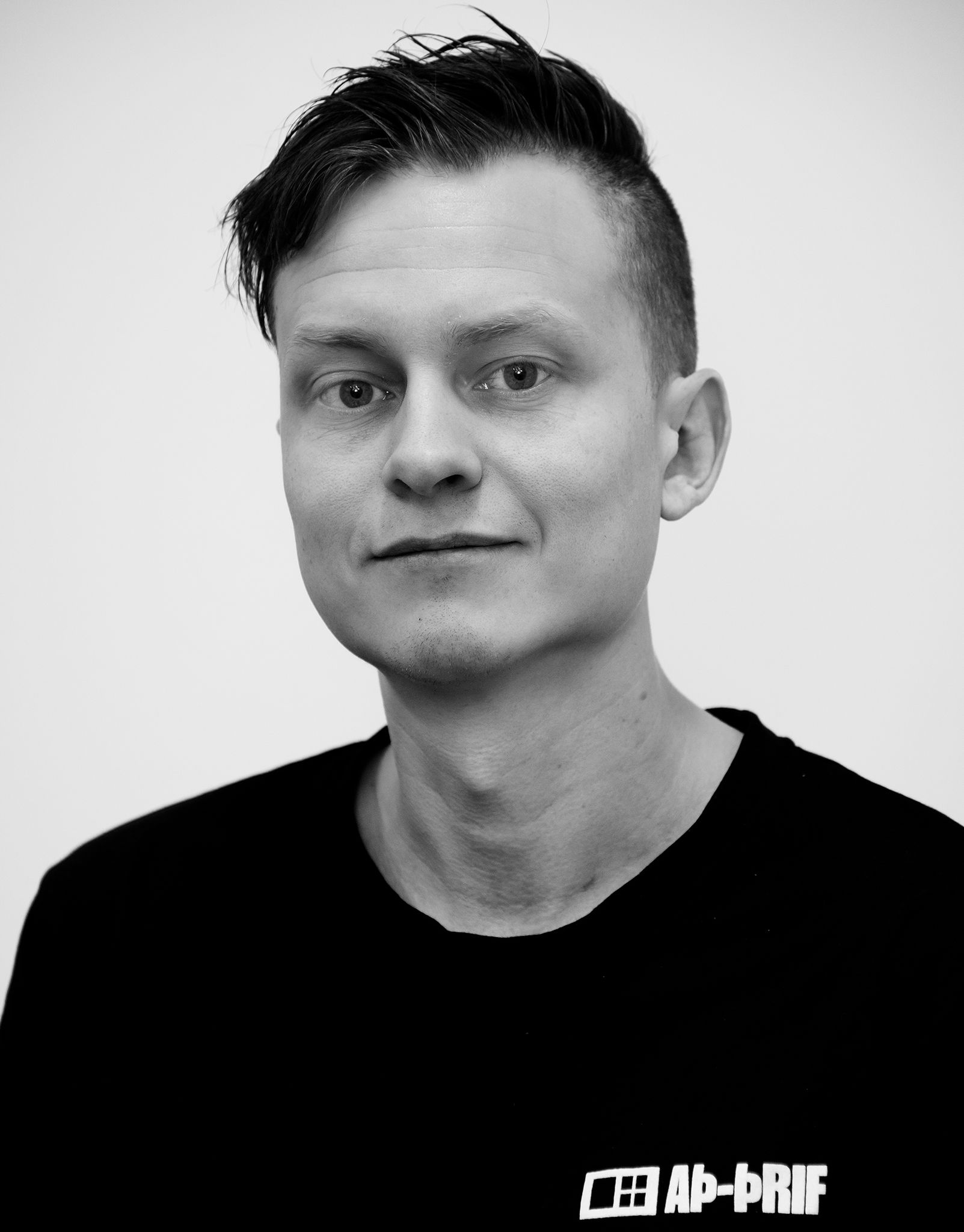 Svart-hvít portrett af manneskju í dökkri skyrtu á einföldum bakgrunni.