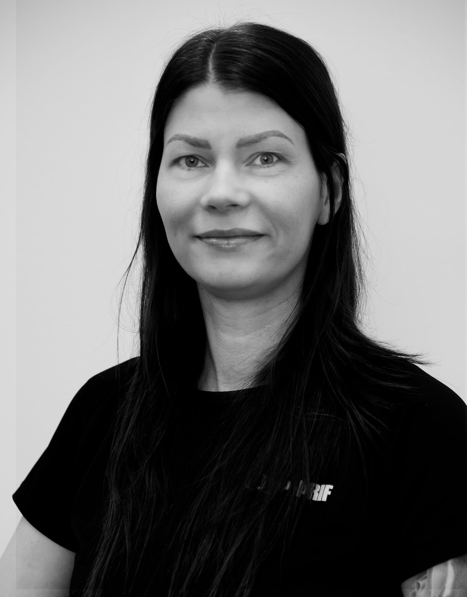 Svart-hvít portrett af konu með sítt dökkt hár, sem snýr fram á við með létt bros.