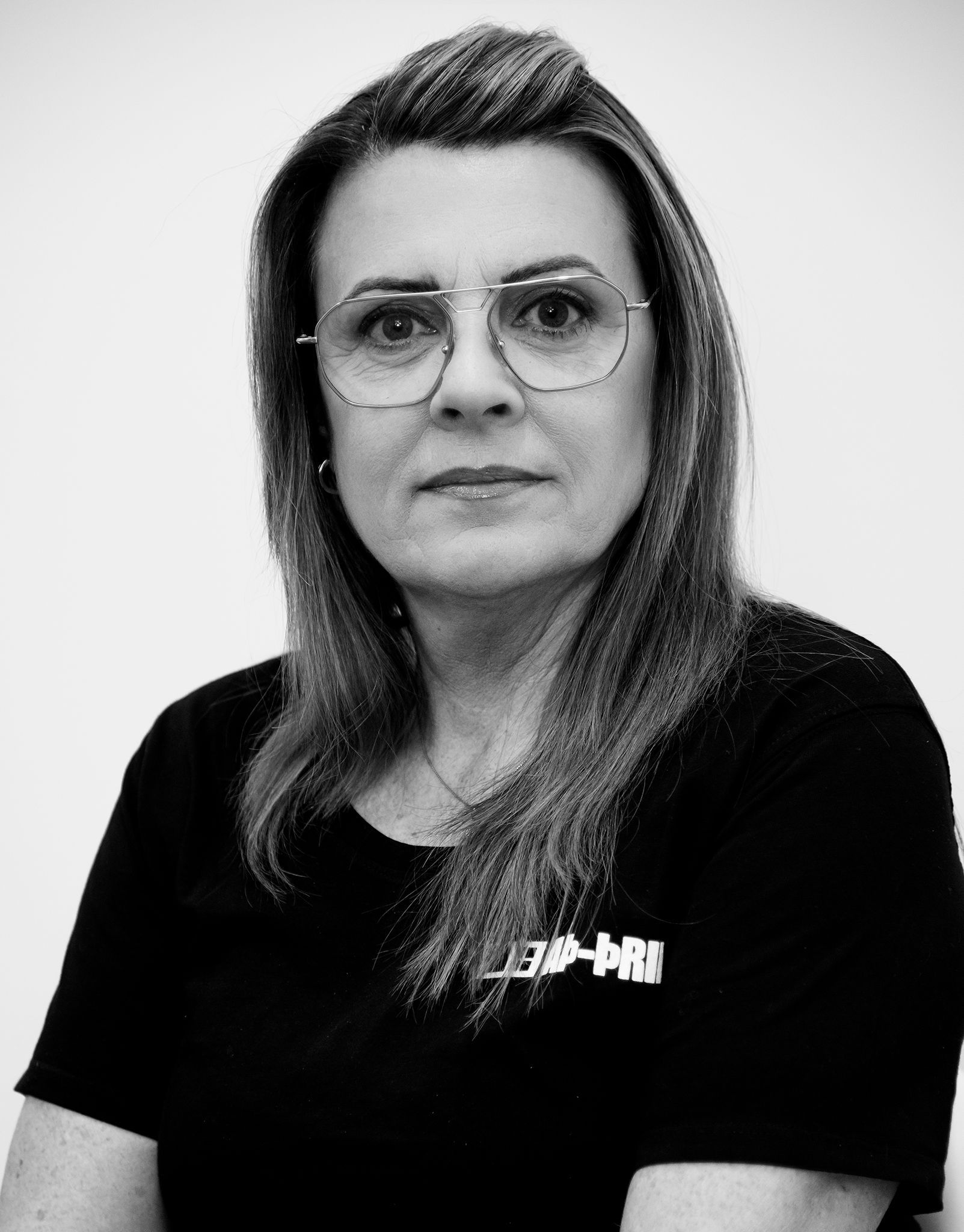 Svart-hvít portrett af manneskju með gleraugu og dökka skyrtu, snýr fram á við með hlutlausu svipbrigði.