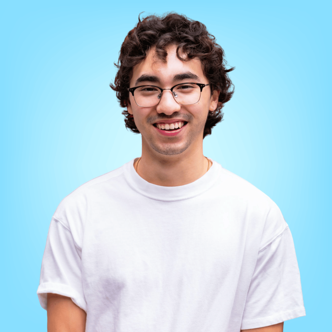 A woman wearing glasses and a plaid shirt is smiling in front of a bookshelf.
