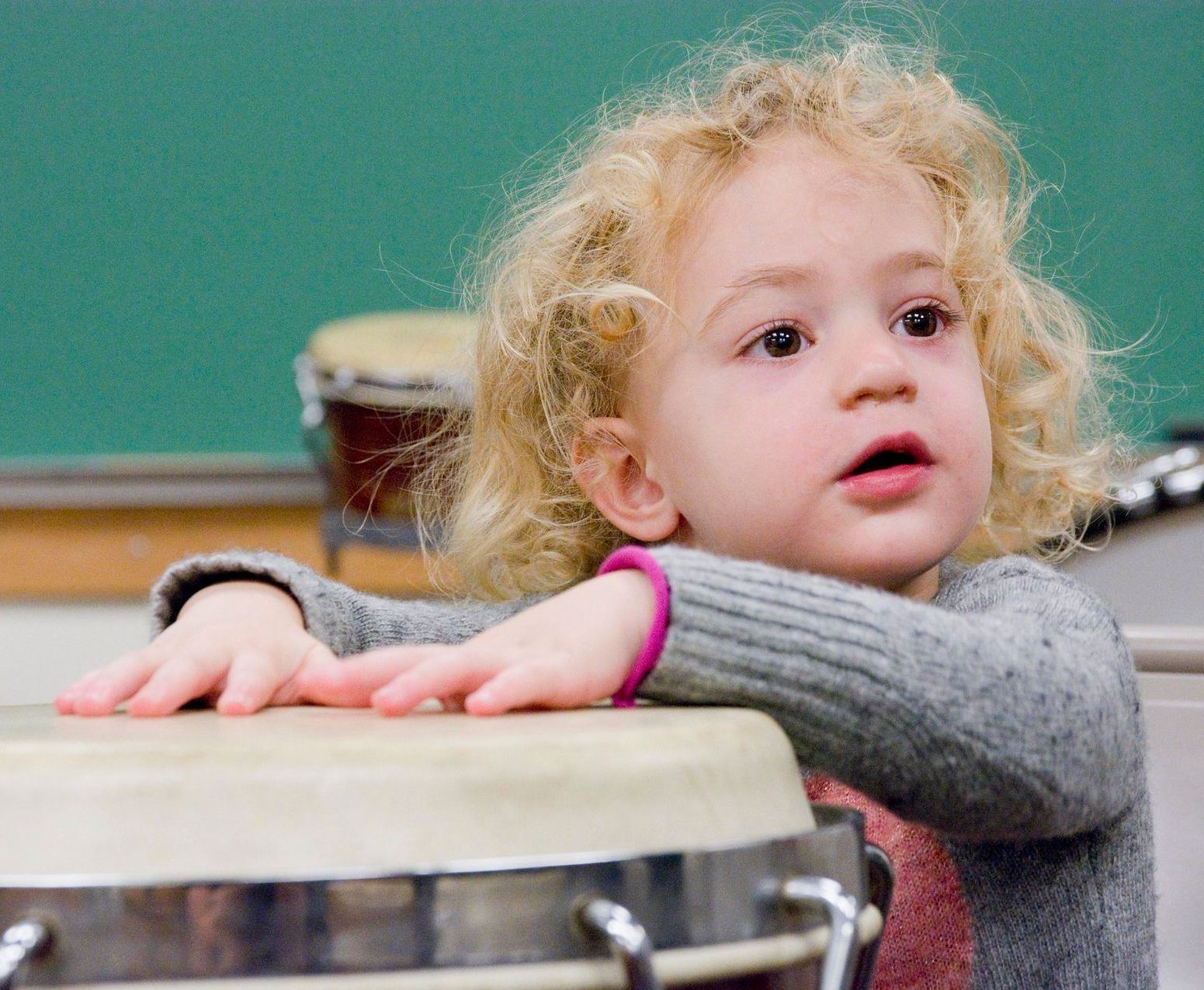 A little girl leaning on a drum in a classroom