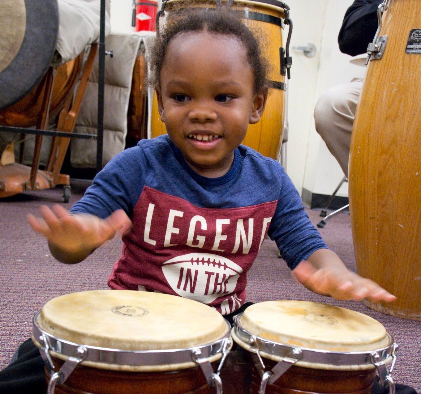A little boy wearing a shirt that says legend is playing drums
