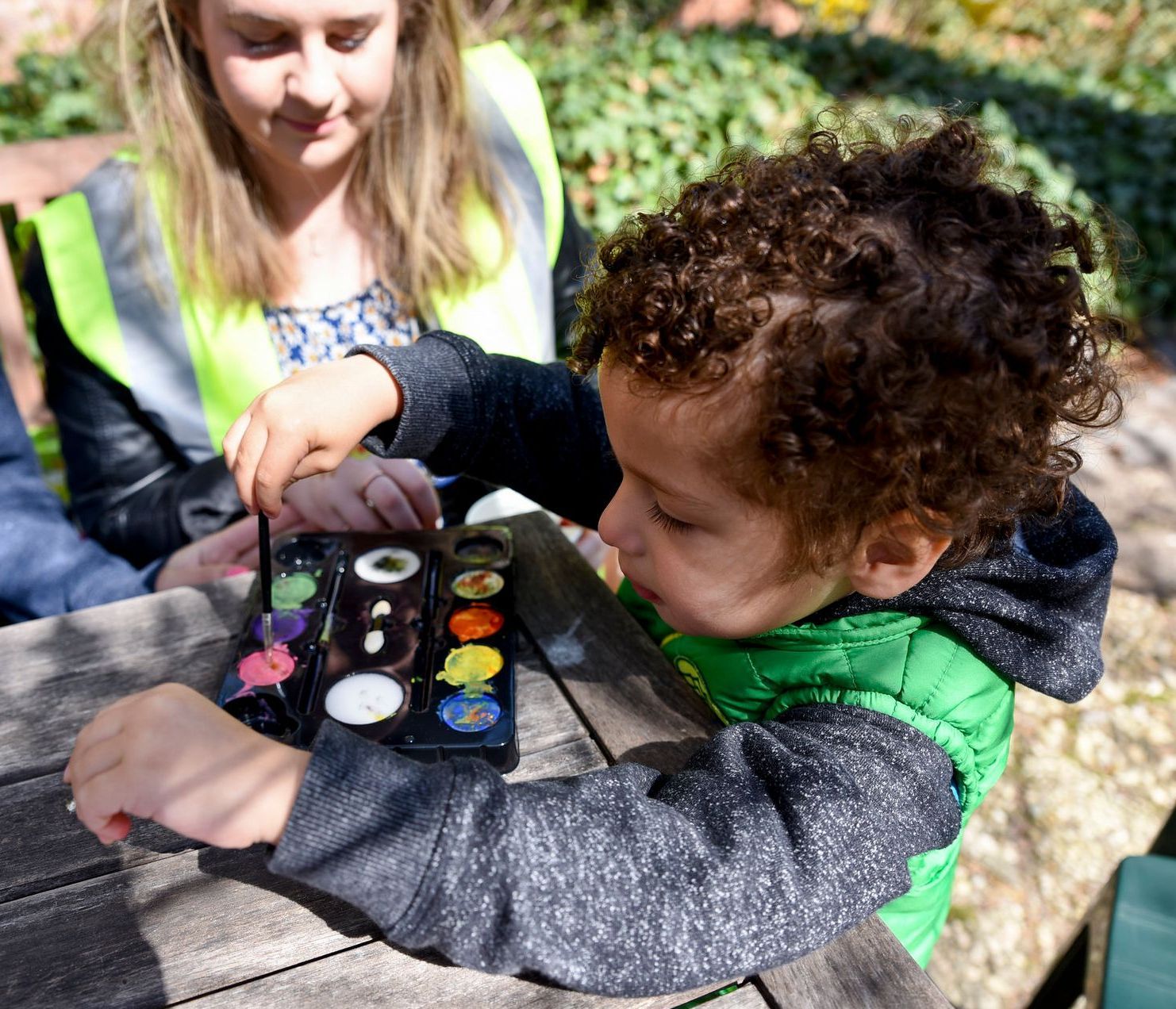 A woman and a child are playing with watercolors on a wooden table.