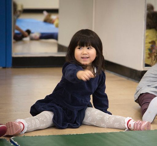 A little girl is sitting on the floor stretching her legs