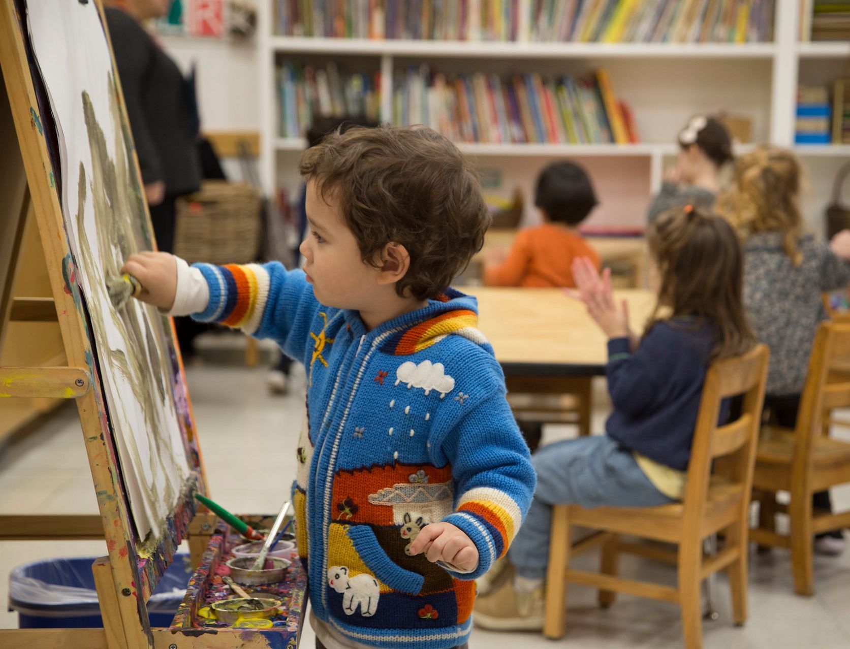 A young boy is painting on an easel in a classroom.