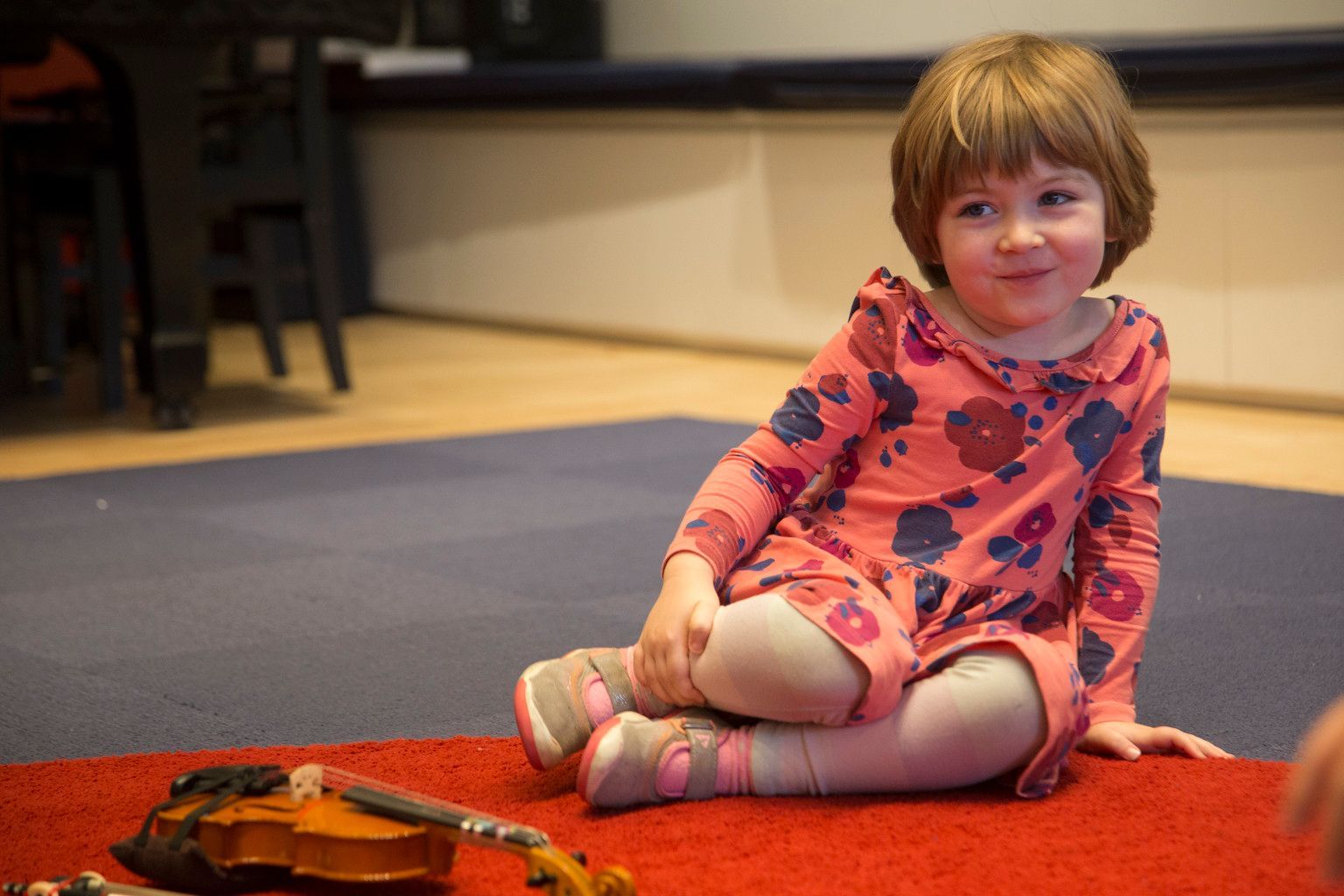 A little girl is sitting on the floor next to a violin.
