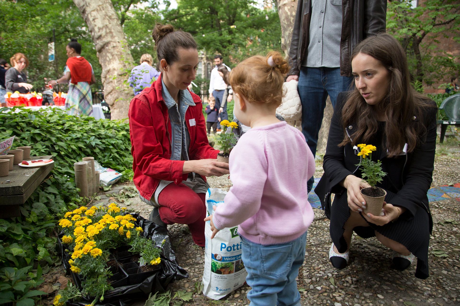 A little girl is standing next to a woman holding a bag of potting soil.