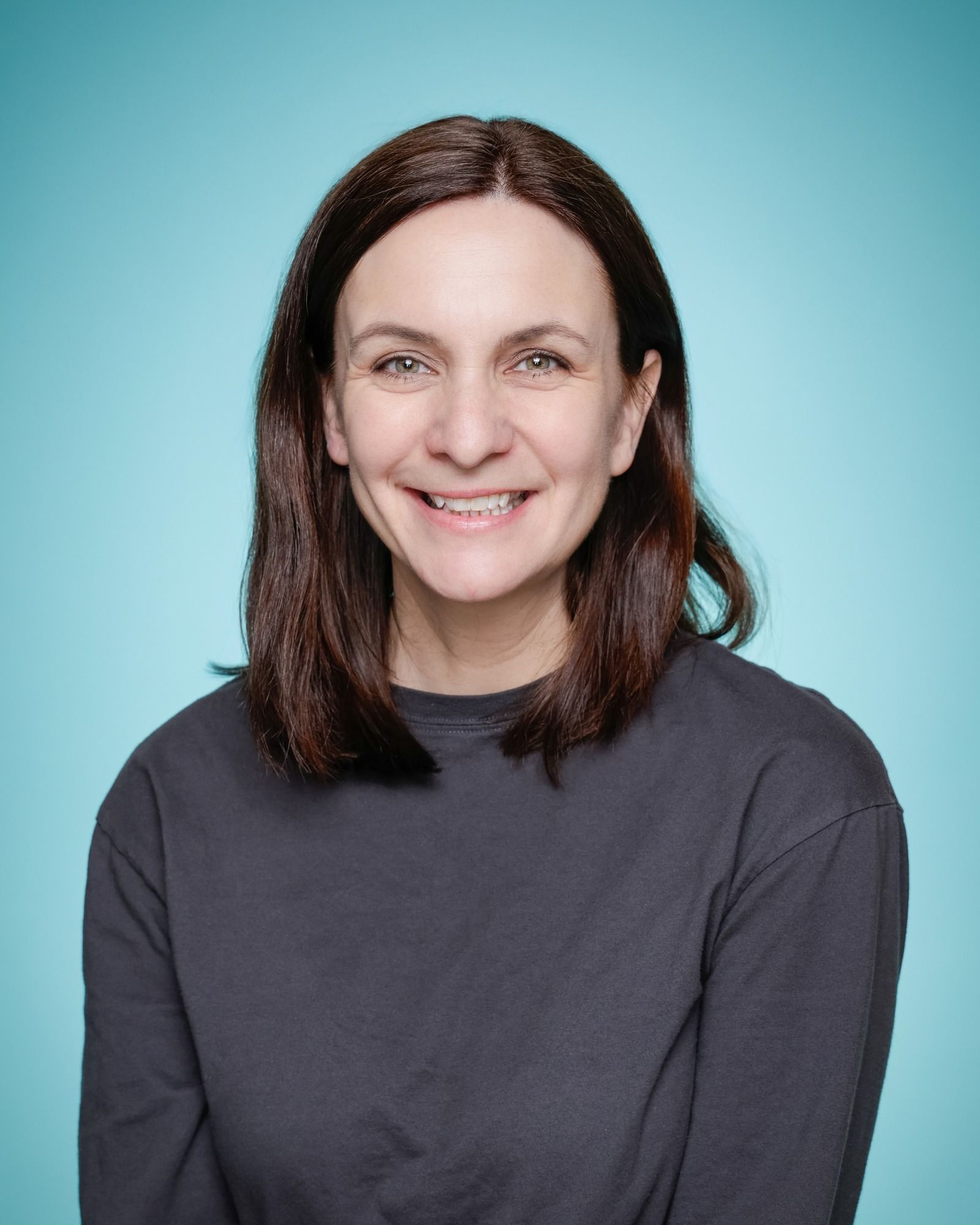 A woman in a green shirt is smiling in front of a bookshelf.