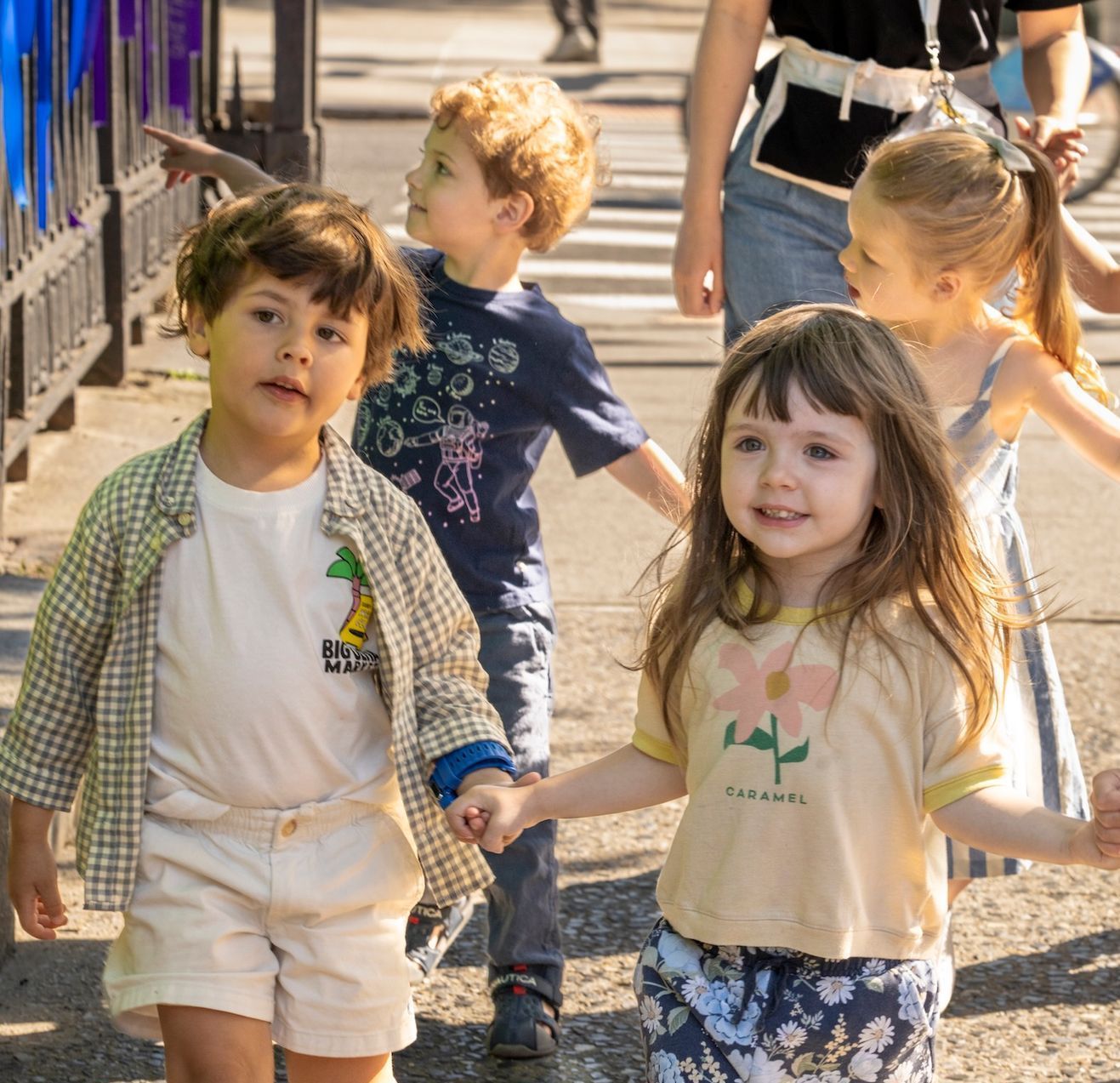 A girl wearing a shirt that says flowers is holding hands with two other children