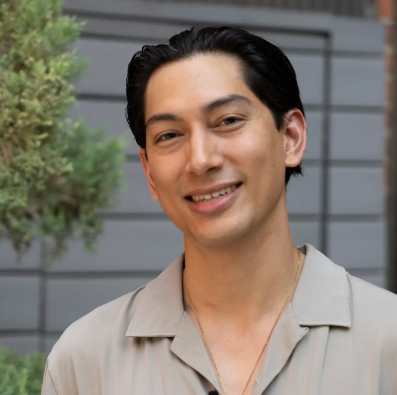 A man in a grey shirt is smiling for the camera