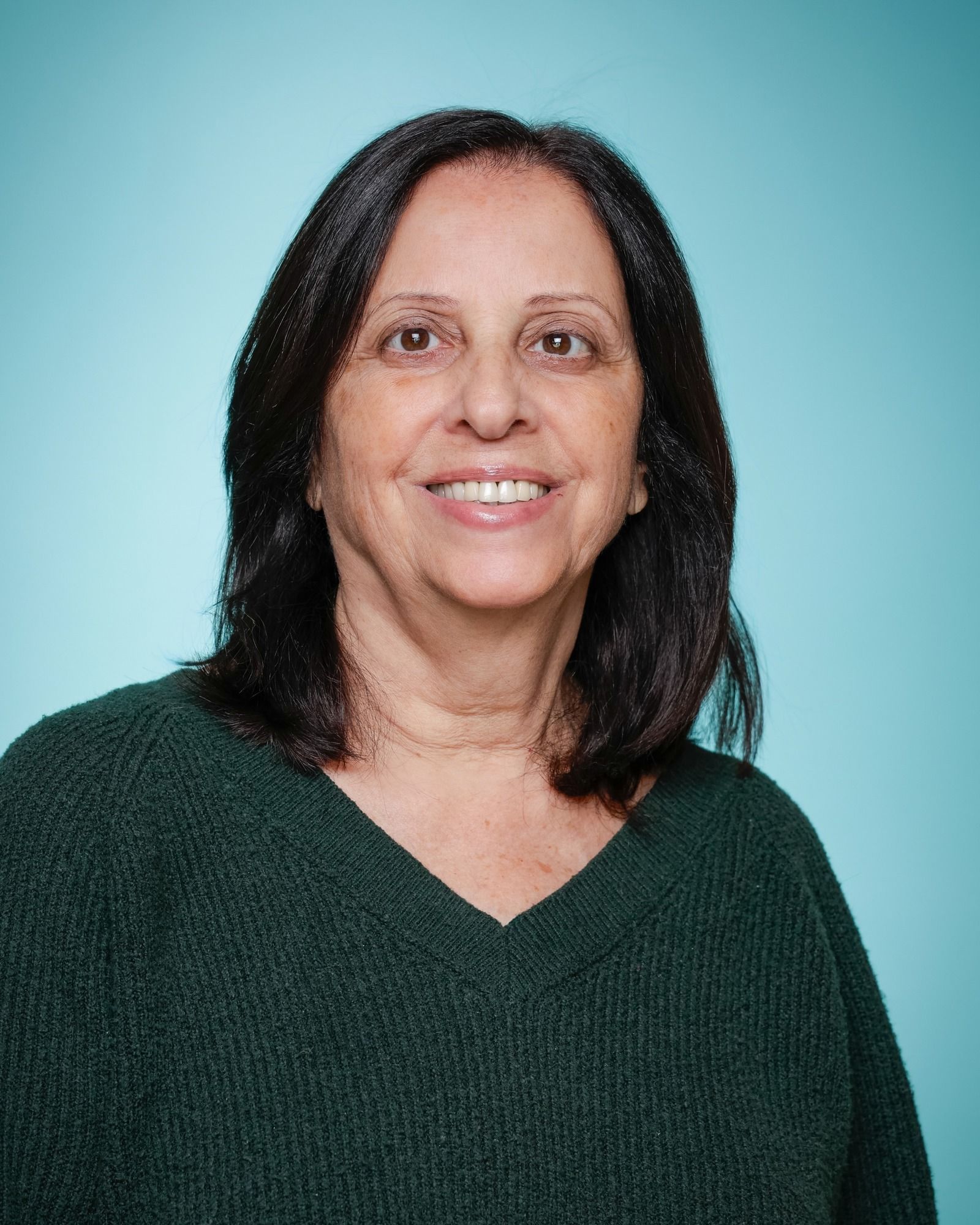 A woman in a blue sweater is standing in front of a bookshelf.