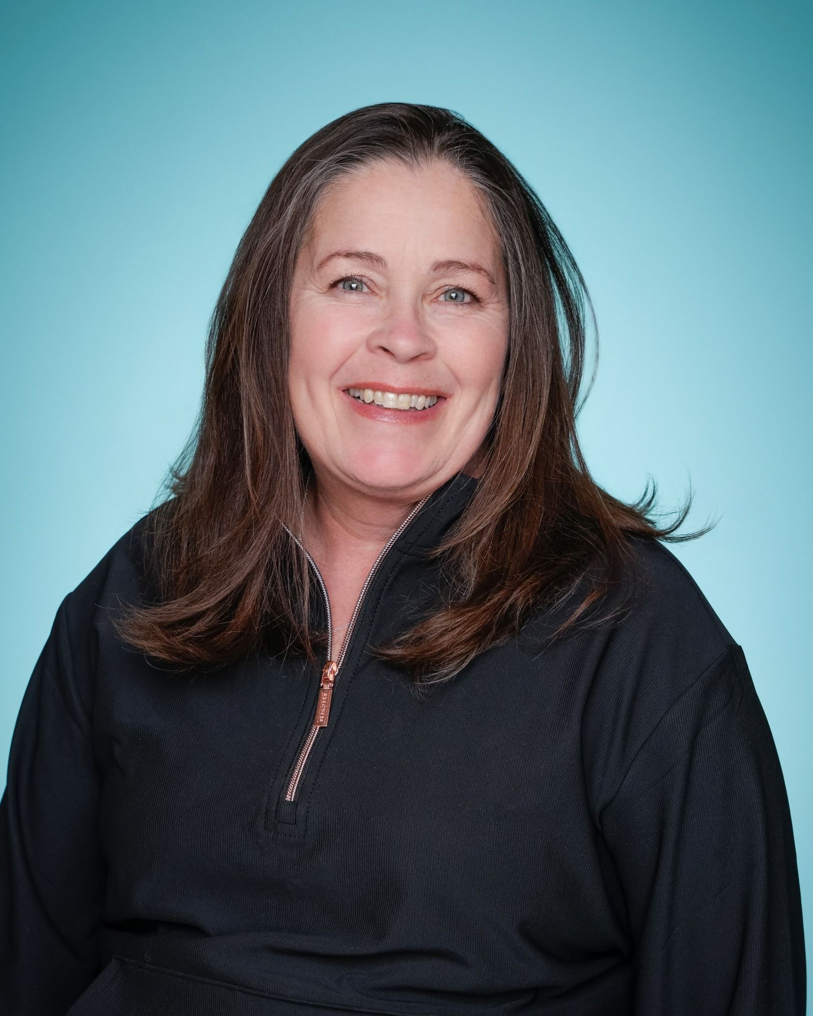 A woman in a green sweater is smiling in front of a bookshelf.