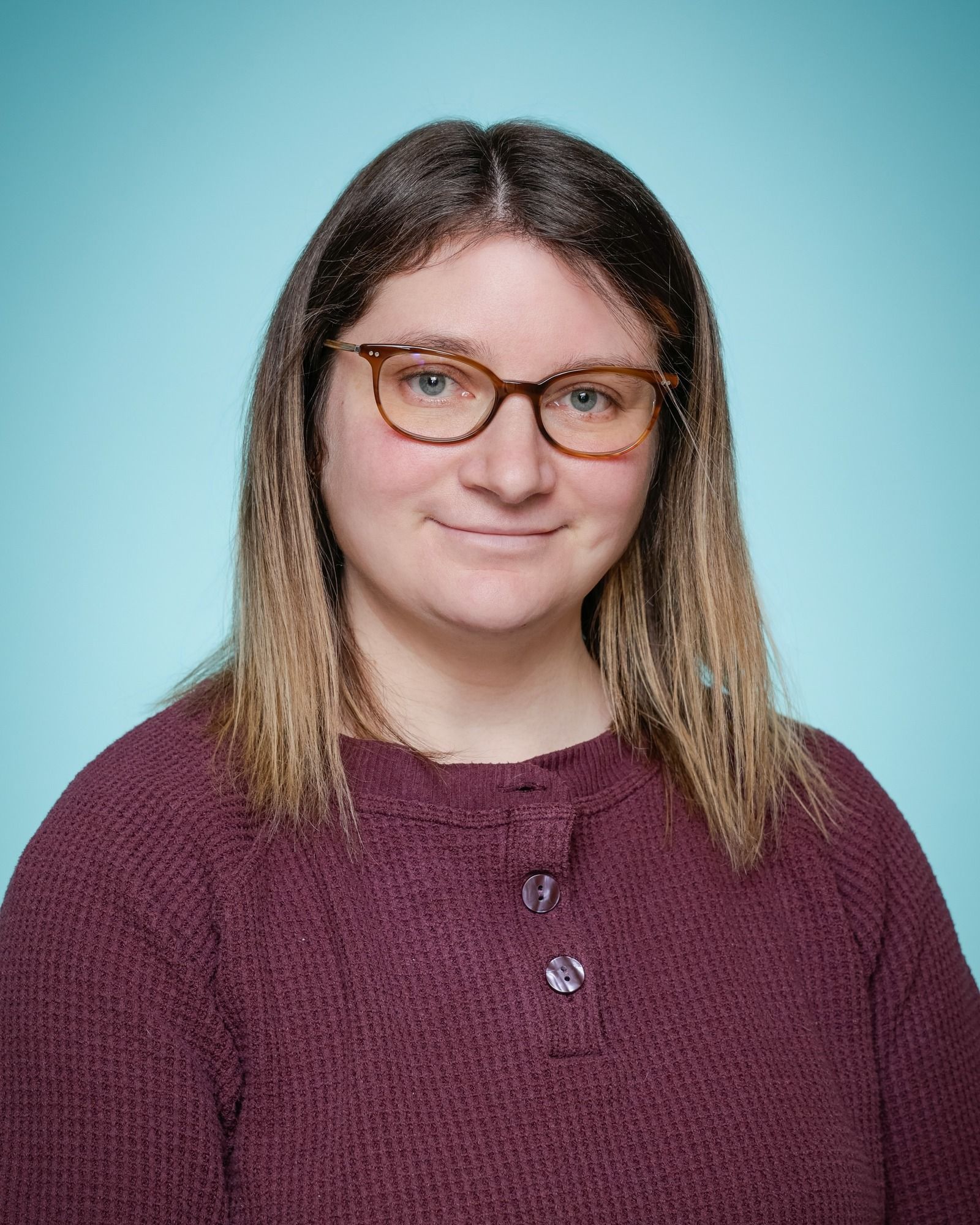 A woman wearing glasses and a lanyard is smiling in front of a bookshelf.