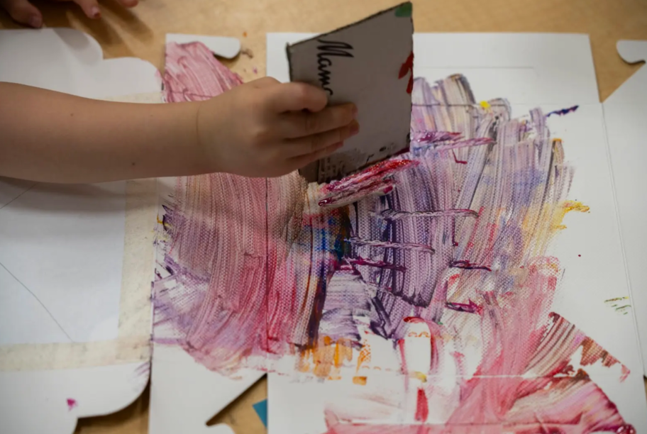 A child is holding a piece of paper over a painting.