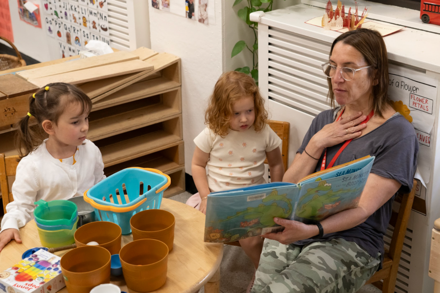 A woman is reading a book to two little girls in a classroom.