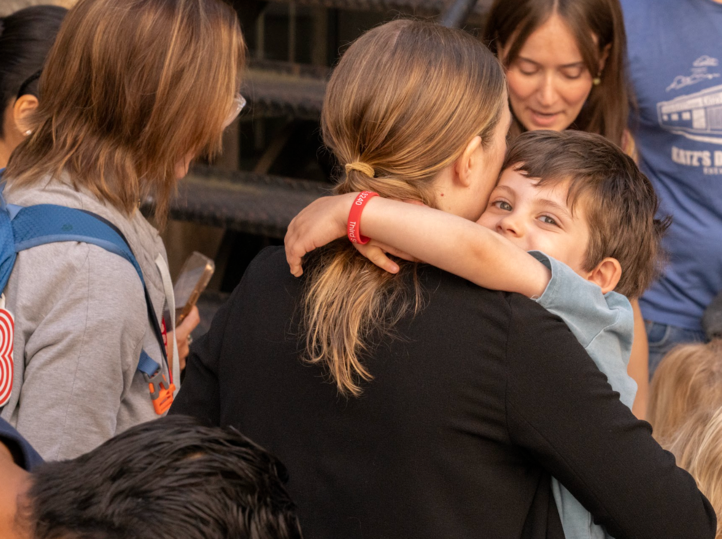 A woman is hugging a young boy in a crowd of people.