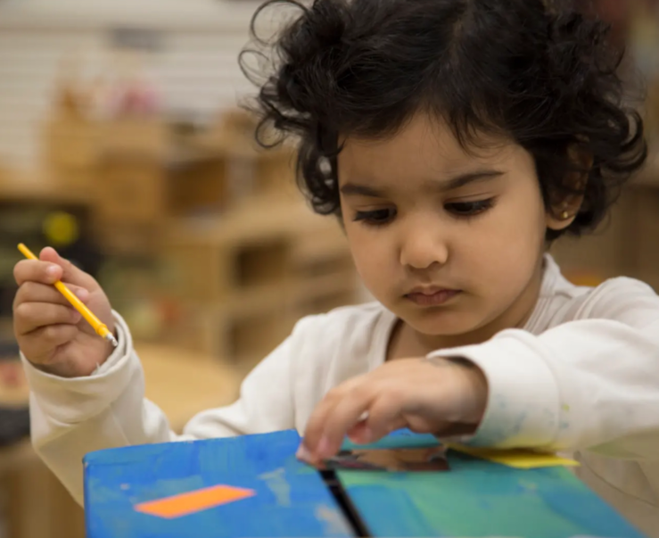 A little girl is holding a yellow pencil in her hand