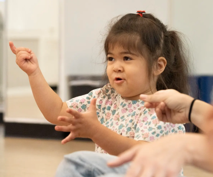 A little girl is sitting on the floor with her hands in the air.