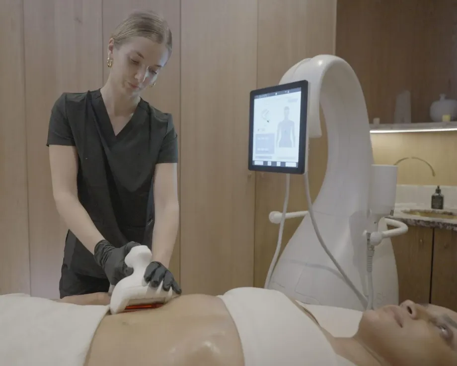 Technician using an Artemis T-Shape 2 device on a client's abdomen in a spa setting.