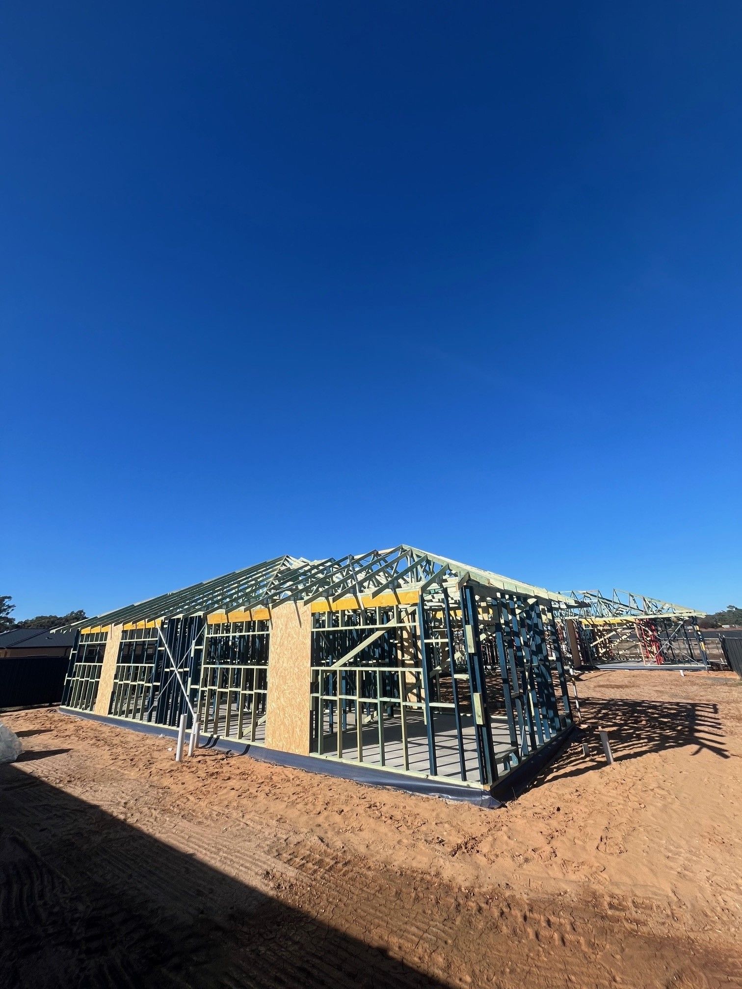 Metal frame of a house under construction against a clear blue sky. 