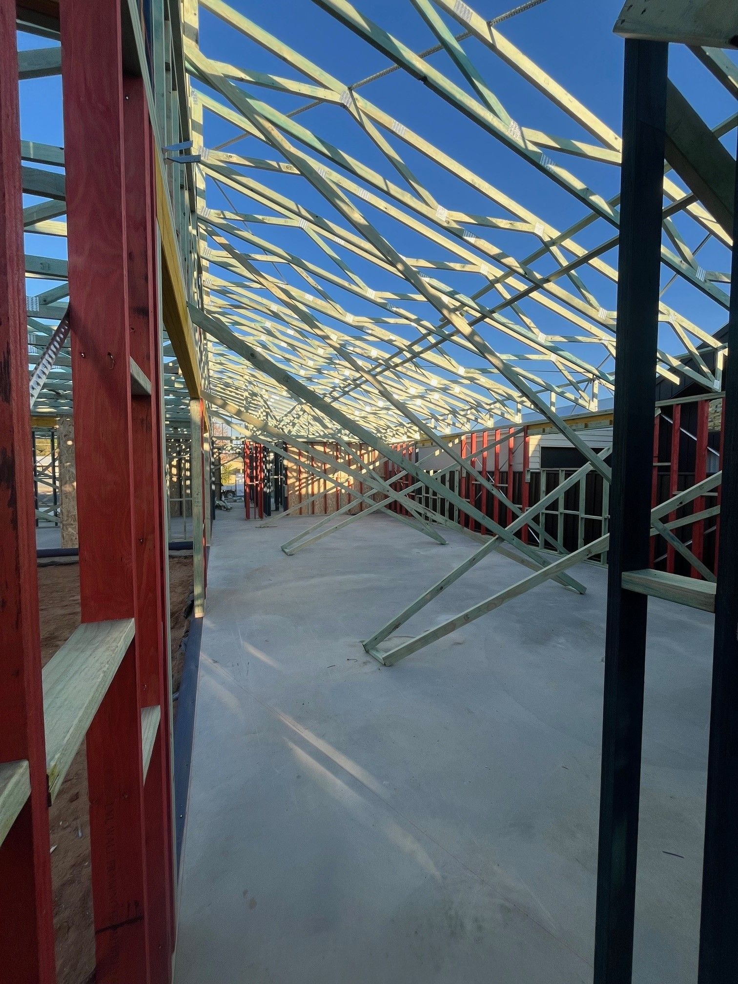 Construction site interior: framing of a building with a concrete floor and a complex roof structure against a blue sky.