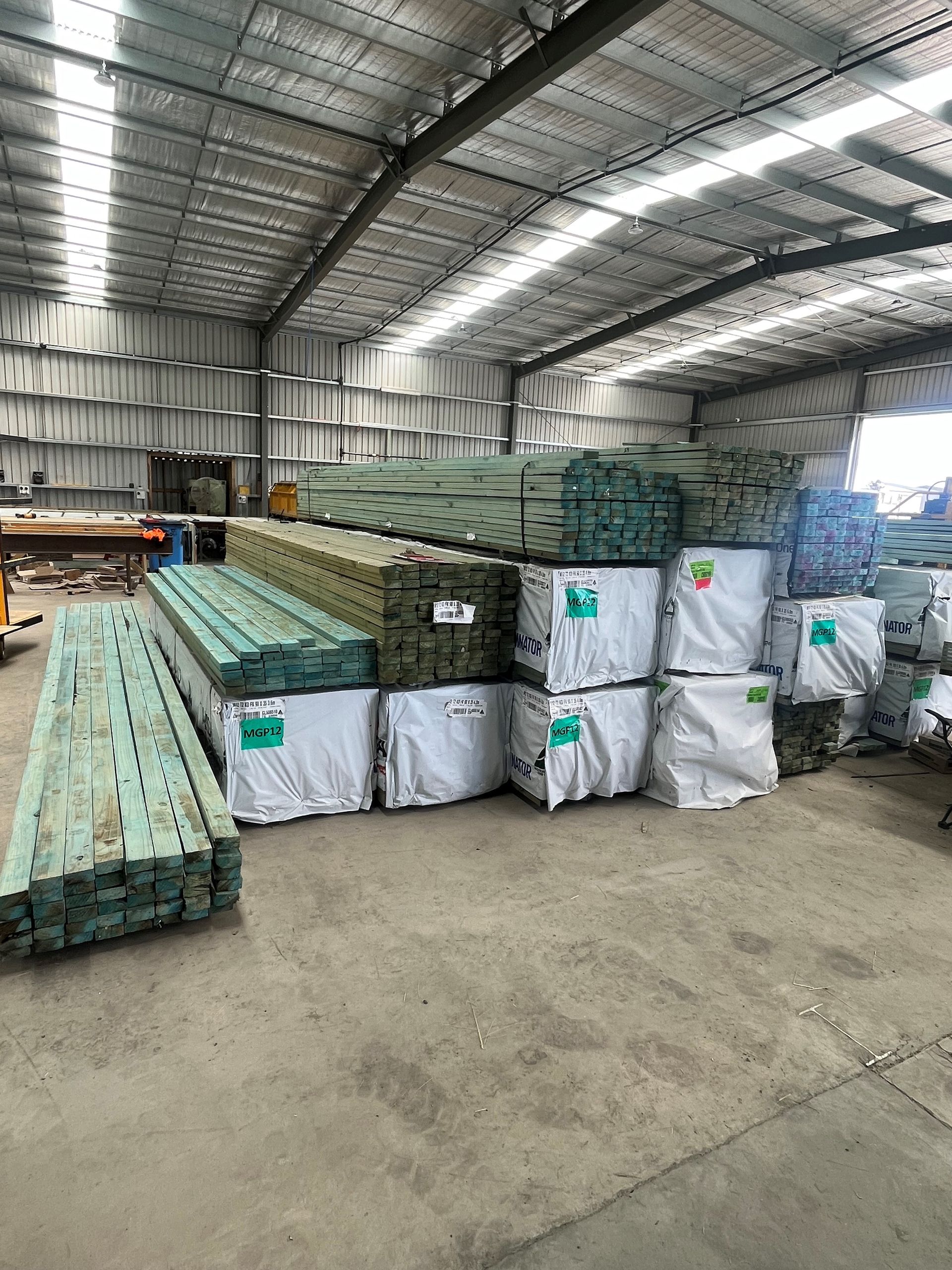 Inside a warehouse, stacks of green-treated lumber are bundled and stored. 