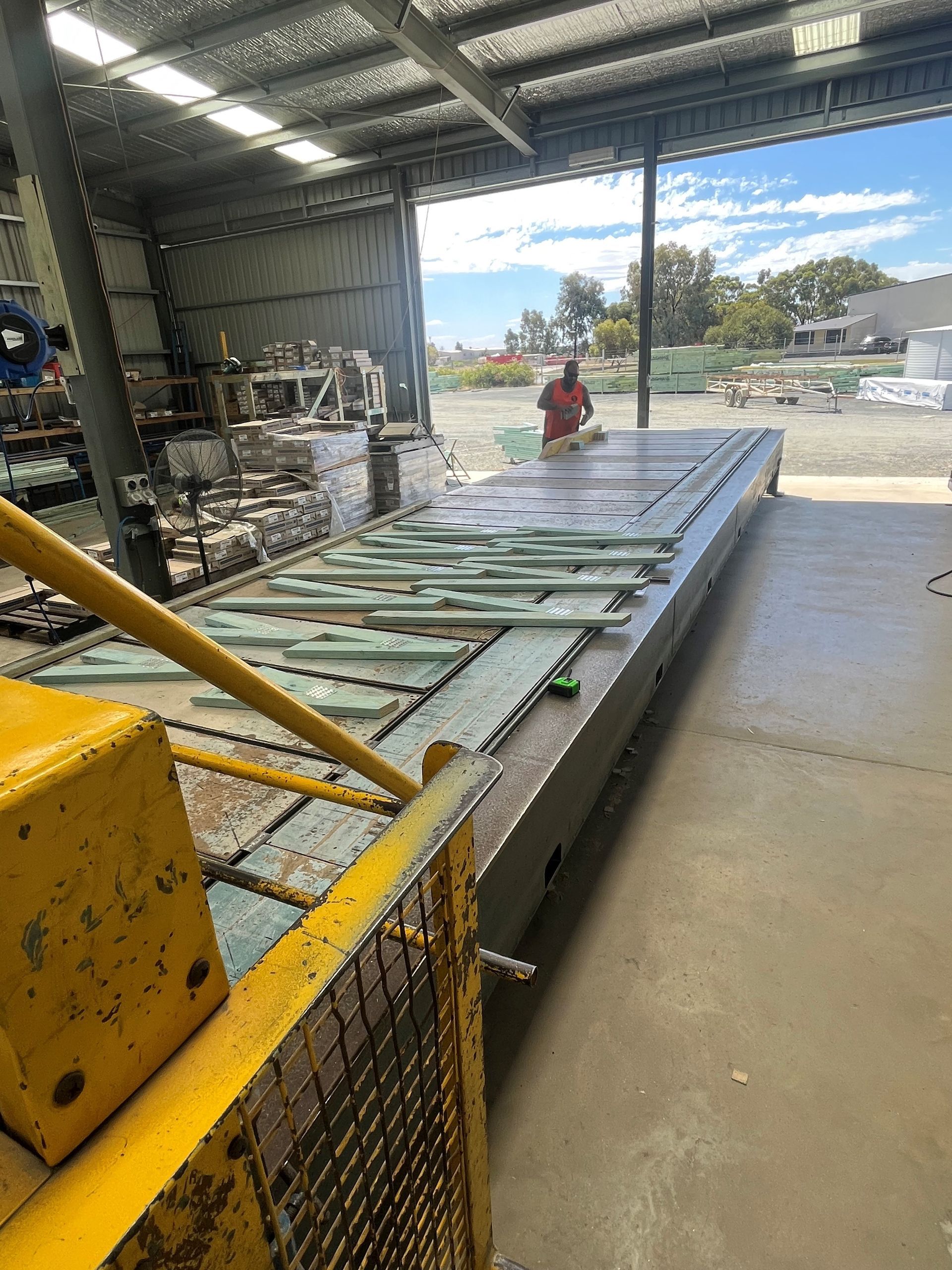 A worker in an industrial setting is working on a large, flat table covered in glass panels. 