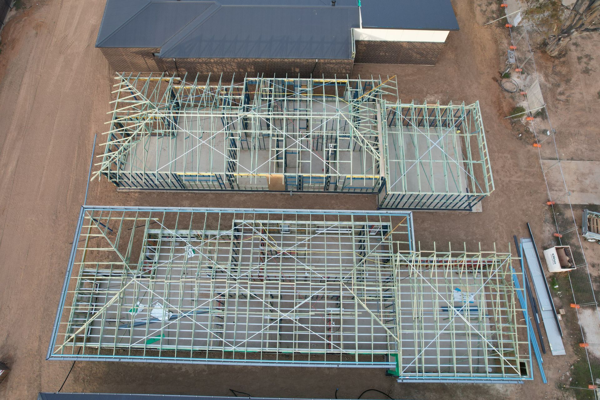 Overhead view of two houses under construction; wood framing outlines rooms on a dirt lot.