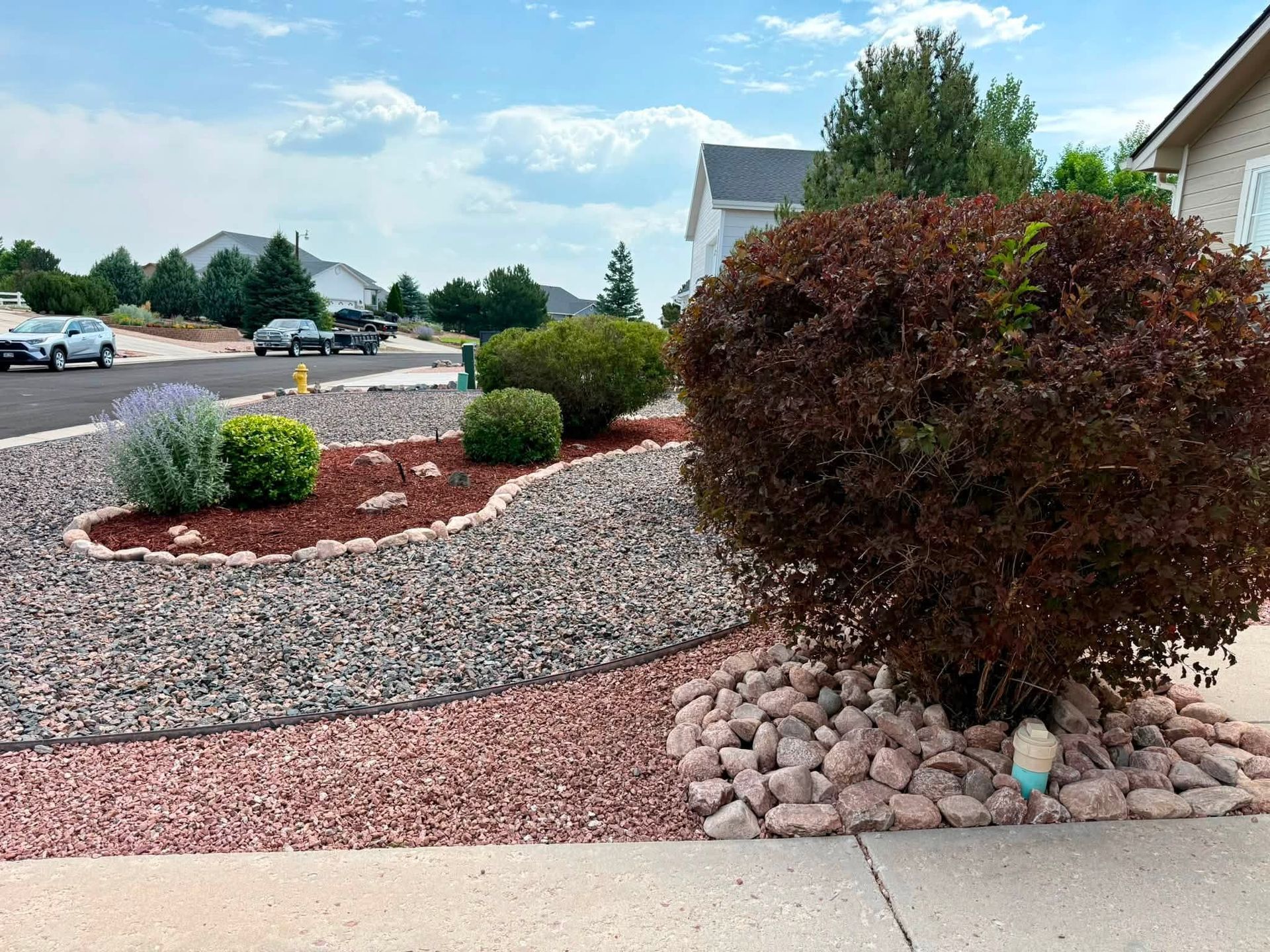 Landscaped suburban front yard with decorative rocks, shrubs, and a driveway under a blue sky