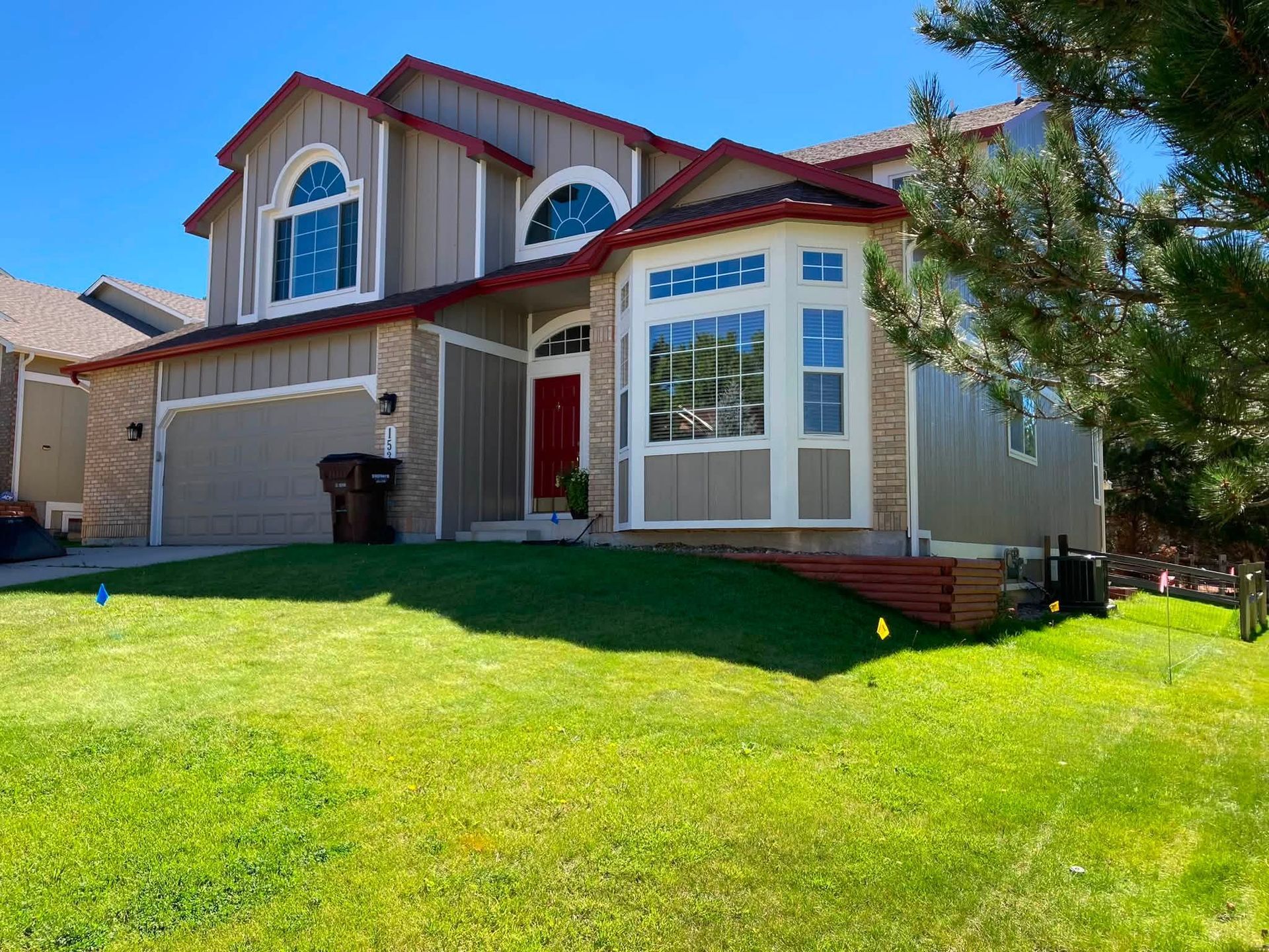 Two-story suburban house with a red front door and green lawn under a clear blue sky