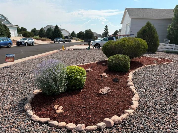 Xeriscaped front yard with red mulch, stone border, and trimmed shrubs beside a suburban street