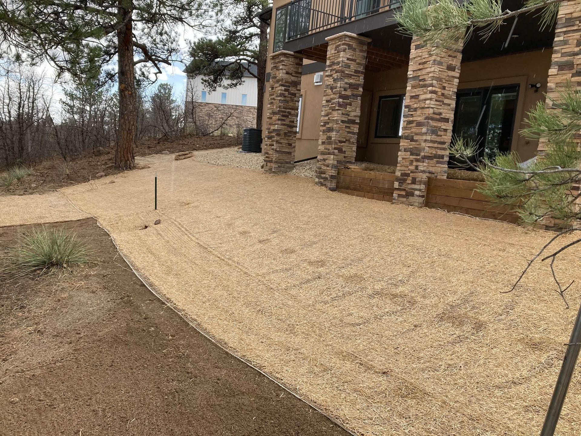 Gravel walkway beside a brick house with stone columns and trees in a wooded yard.