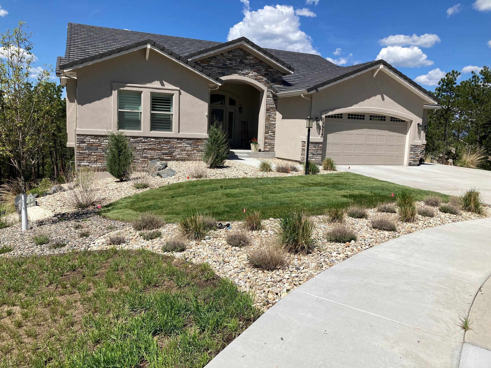Single-story beige house with stone accents, two-car garage, and a curved driveway under a blue sky