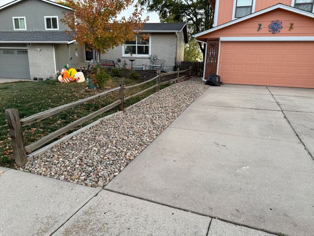 Driveway beside a small garden bed with autumn leaves and a peach-colored garage