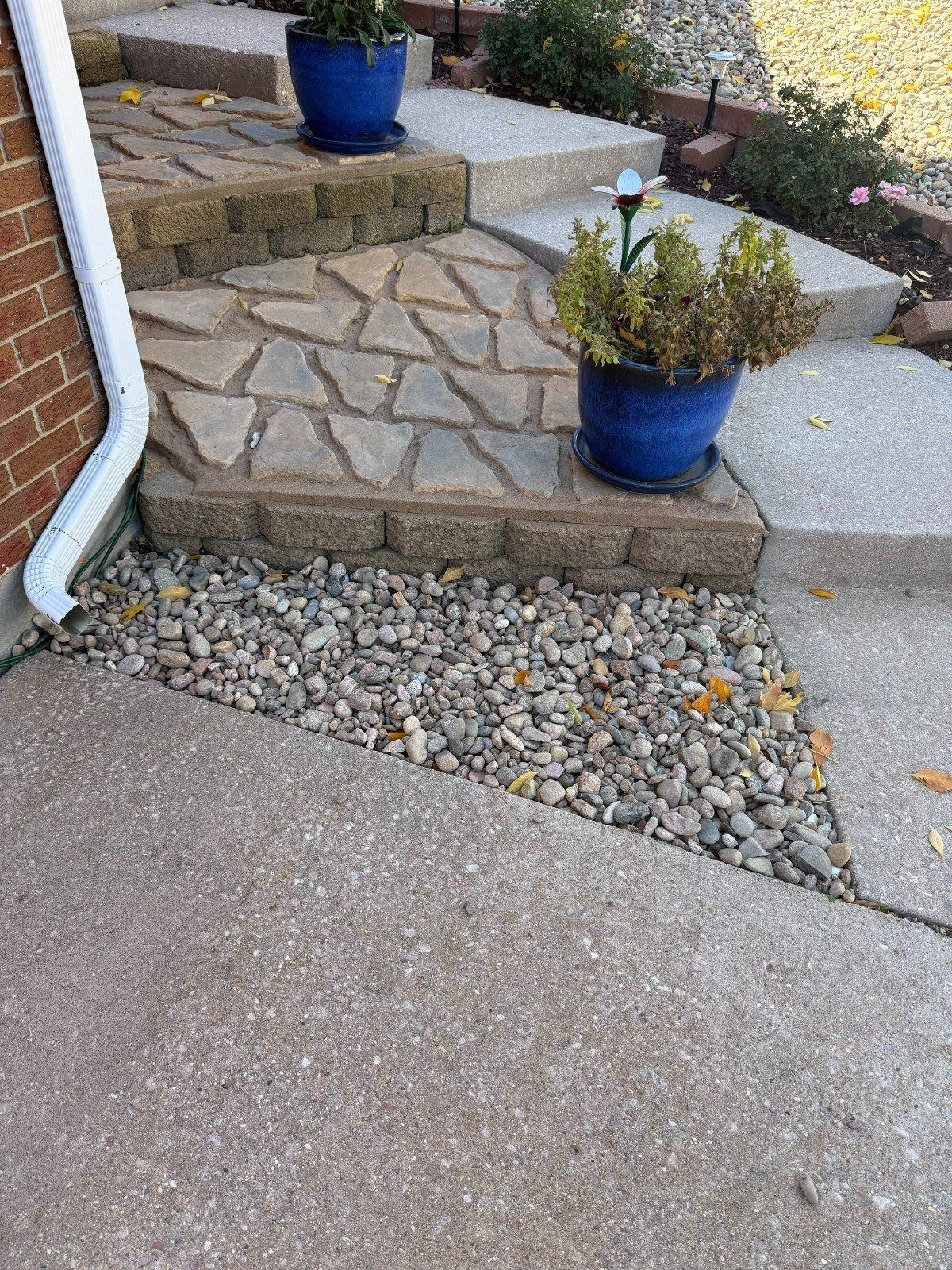 Stone steps and walkway beside a house, with blue flower pots and a gravel strip.