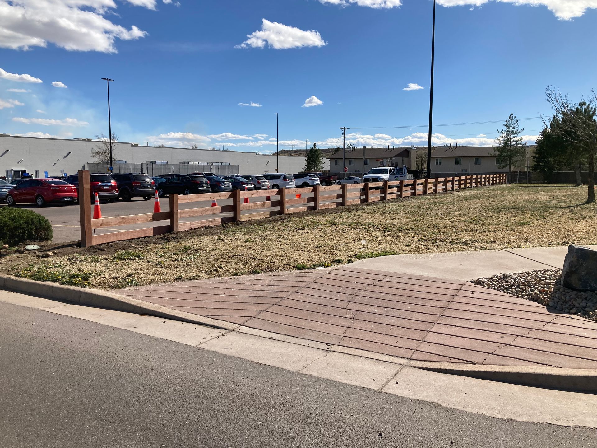 Parking lot with red brick walkway, low fence, and blue sky with clouds