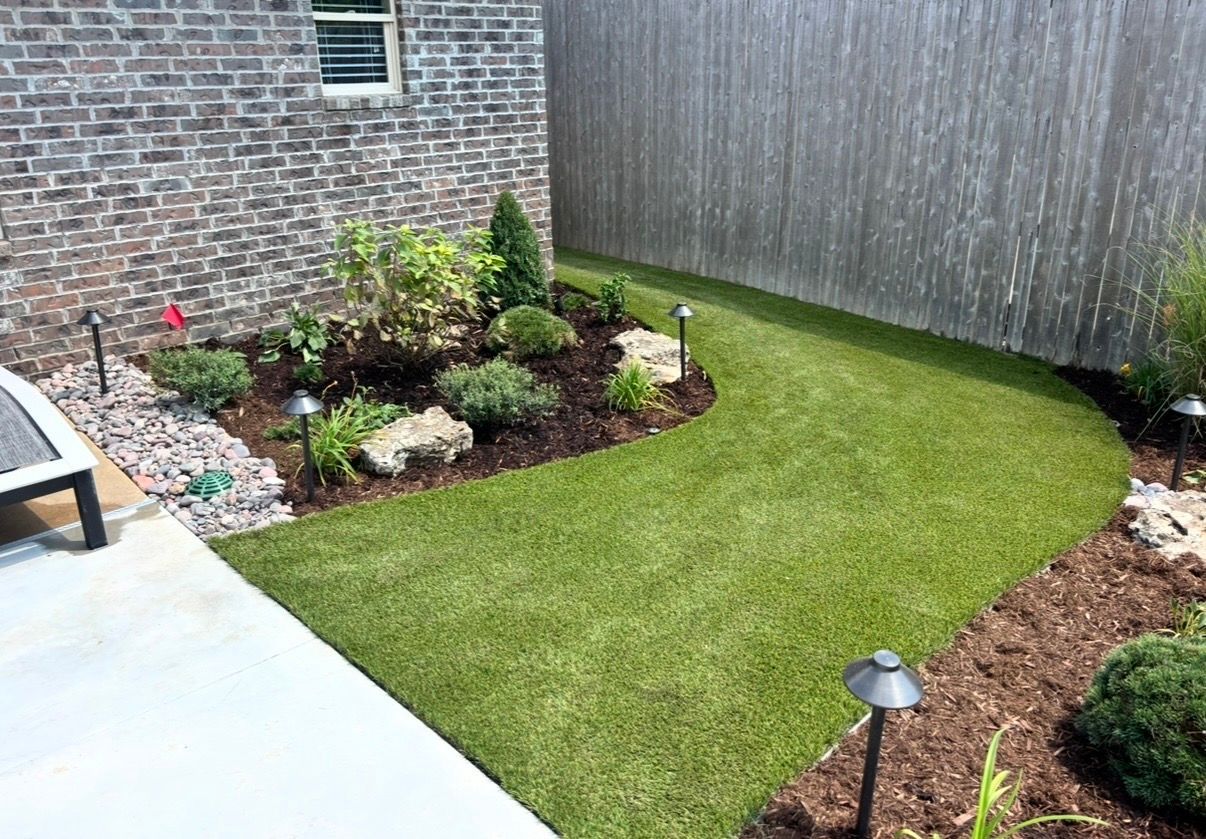 Curved backyard lawn with brick house wall, landscaped flower beds, and a small path light