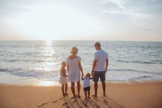 A family is standing on a beach holding hands and looking at the ocean.