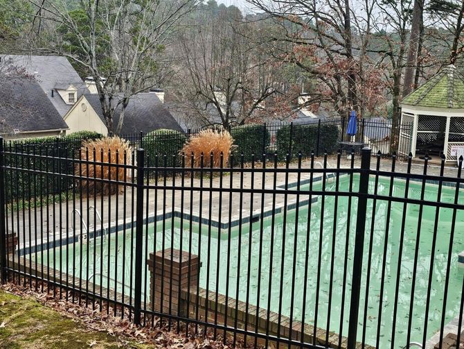 A black fence surrounds a swimming pool in a backyard.