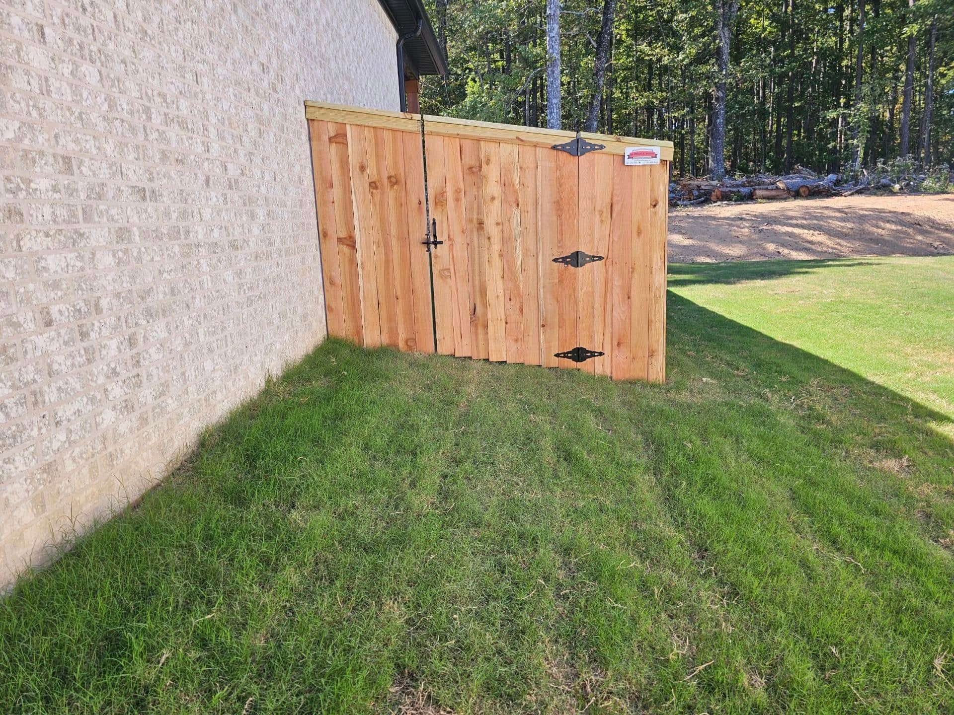 A wooden fence is sitting in the grass next to a brick wall.