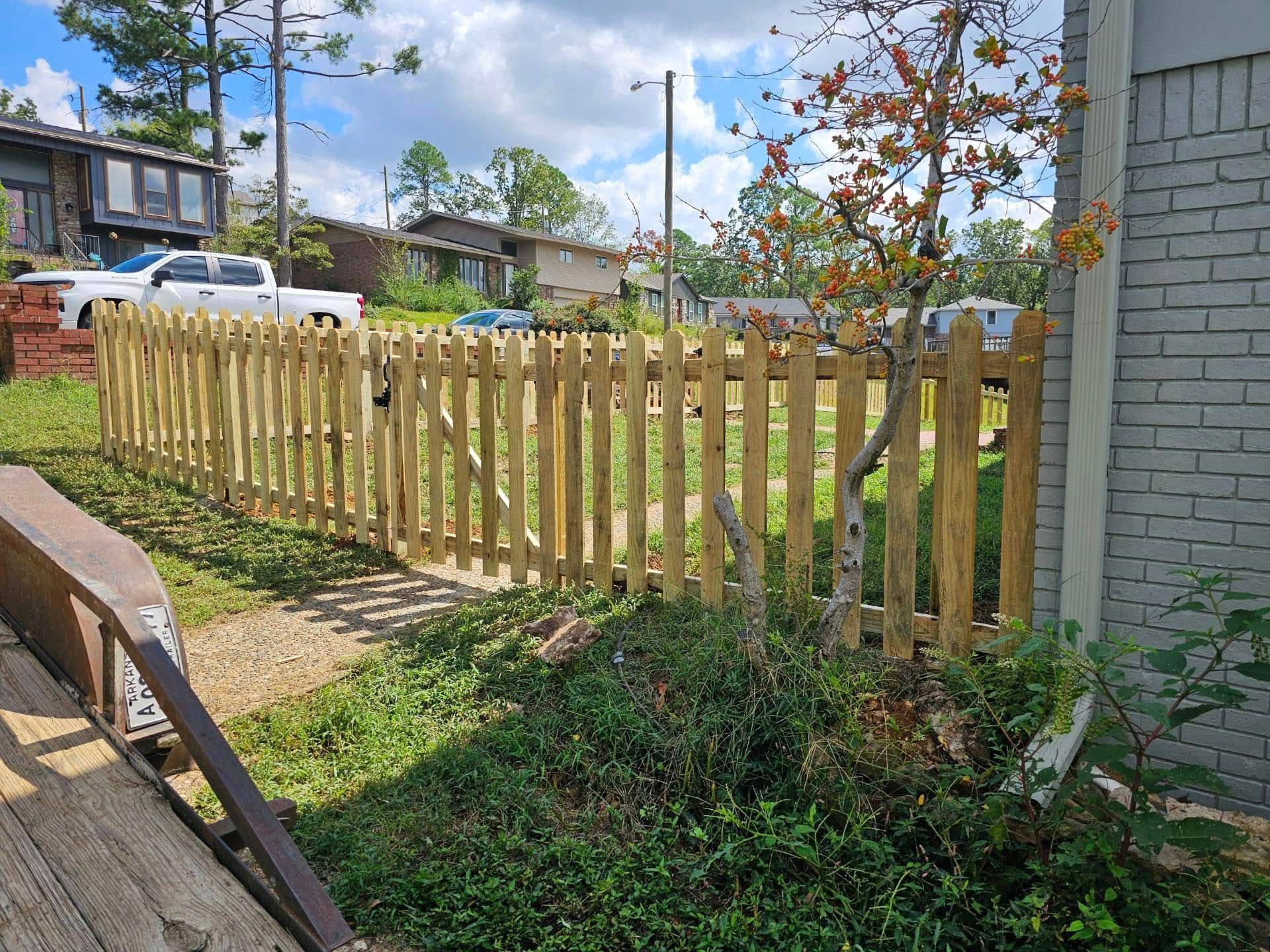 A wooden picket fence is in front of a brick building.