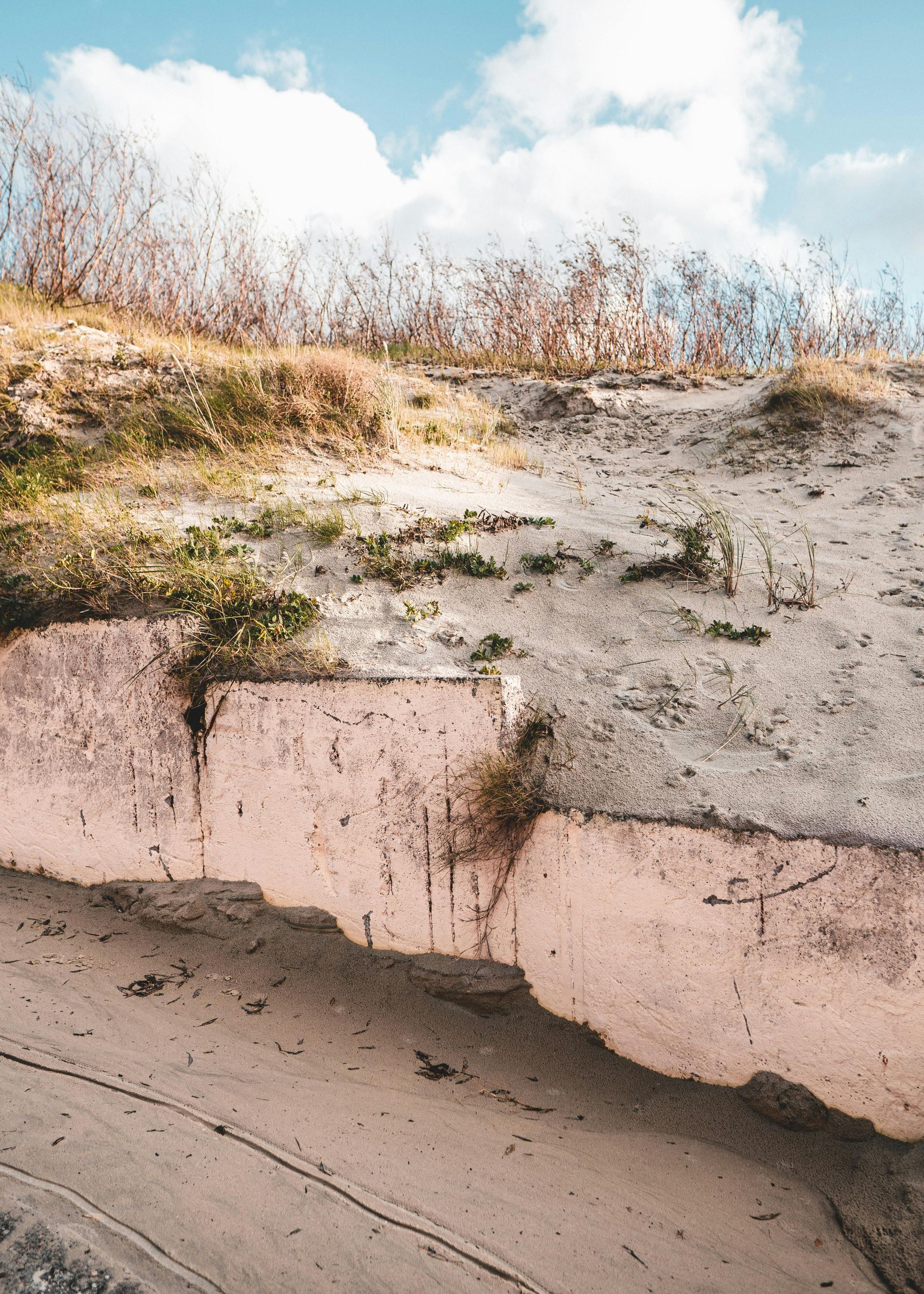 Eroded sandy cliff with dry grass and a cloudy blue sky above a sloped dirt embankment