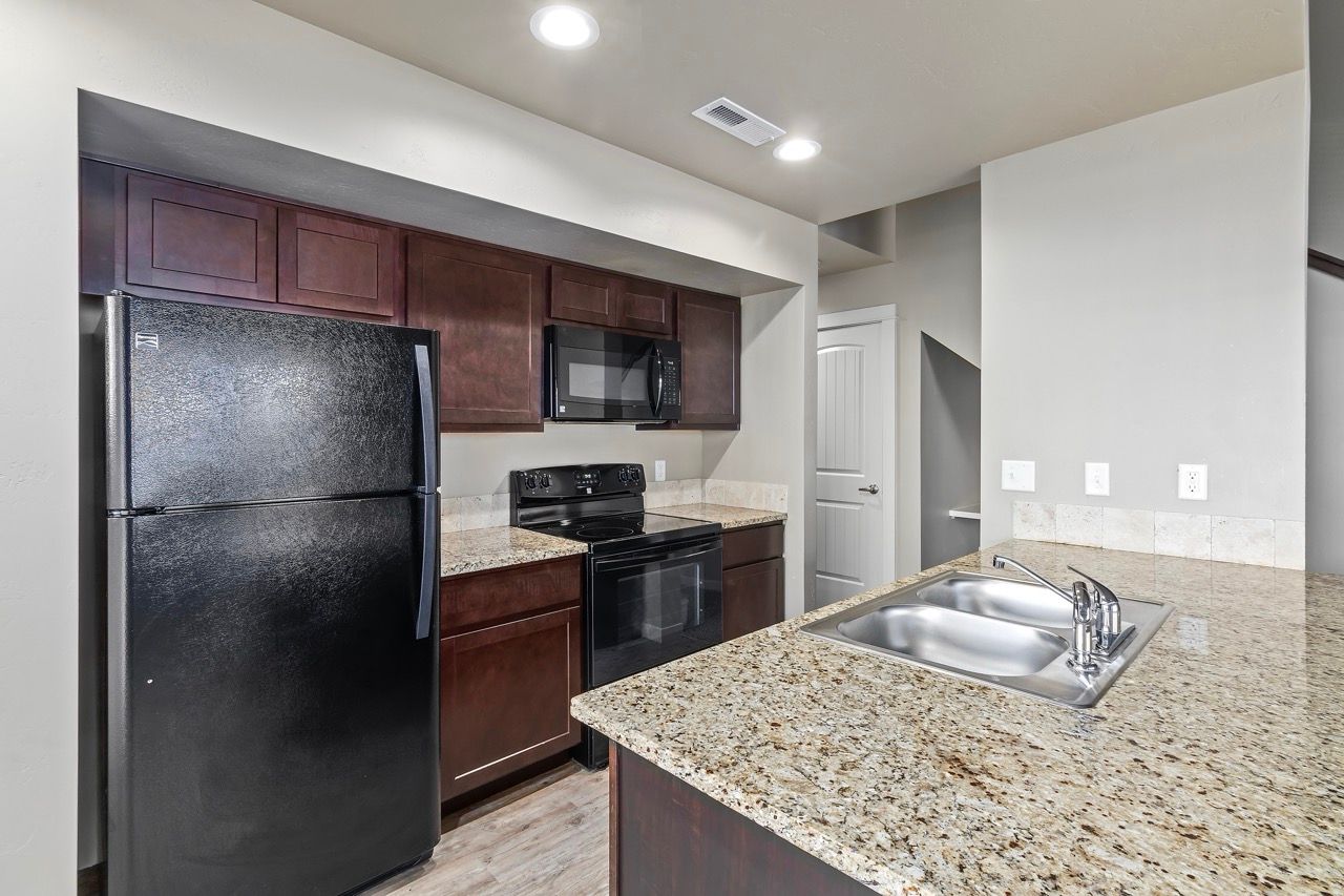 Apartment kitchen with dark wood cabinets, granite countertops, black appliances, and a double sink.