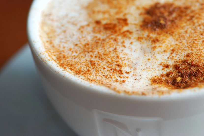 Tazza bianca di cappuccino spolverato di cannella, su un piattino