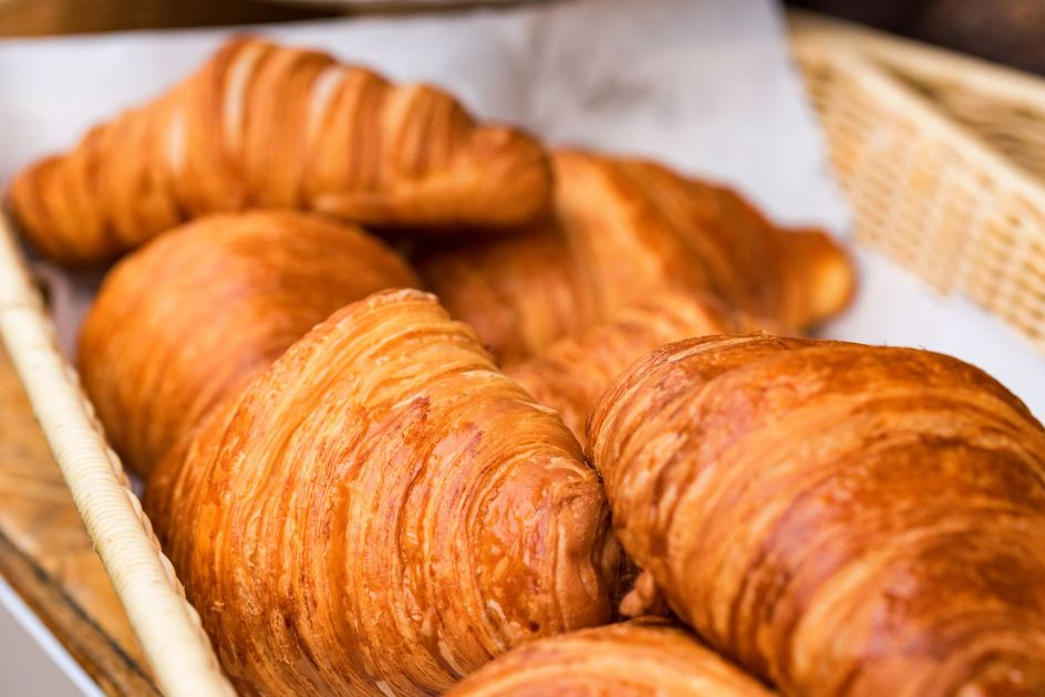 Cestino di croissant dorati disposti su carta da forno bianca