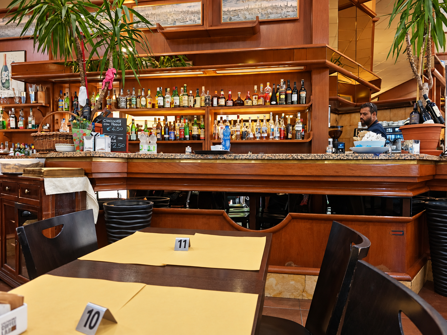 Ristorante-bar con scaffali di liquori, tavoli in legno e piante da interno