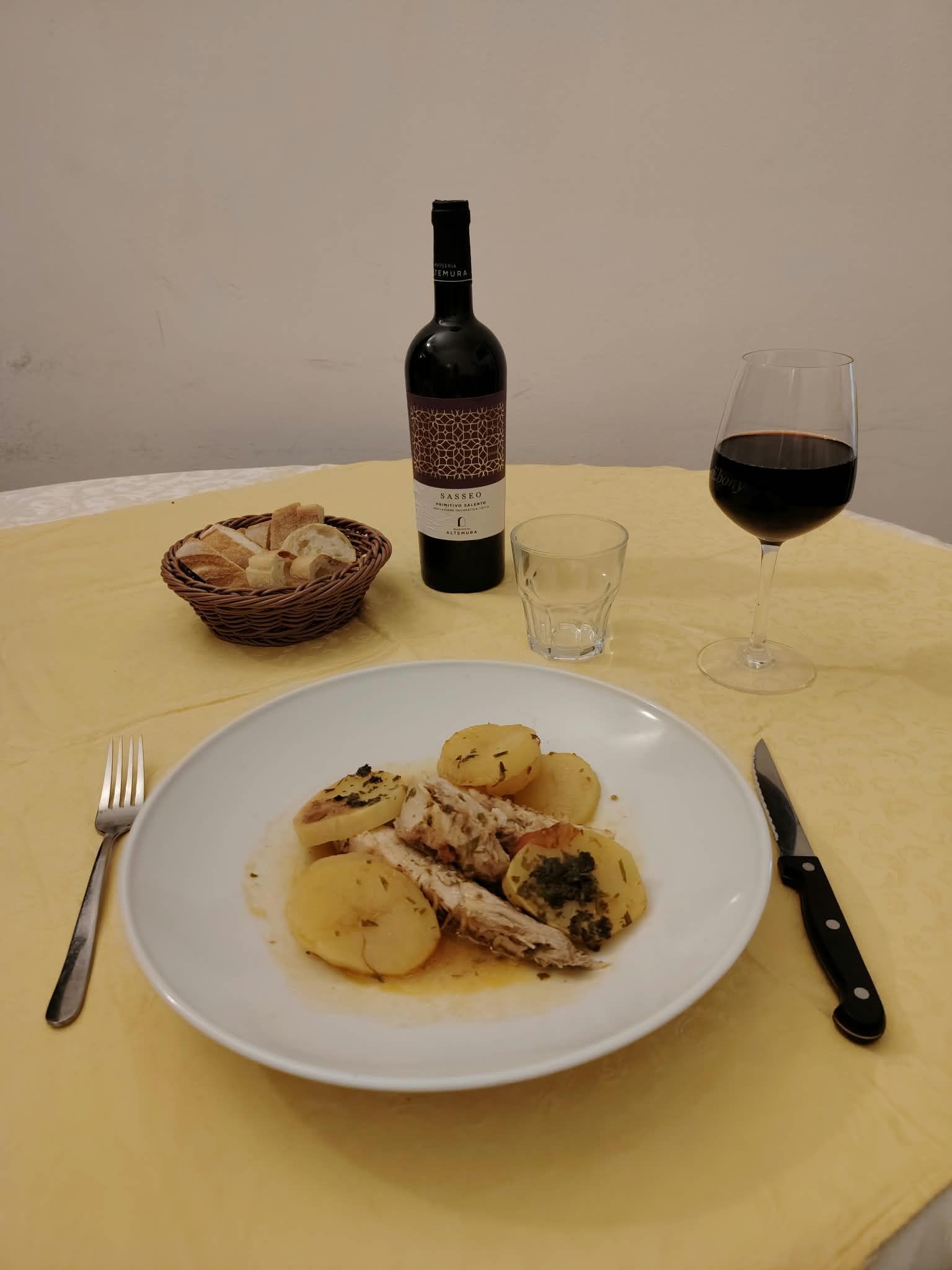Una bottiglia di vino, un bicchiere e un piatto servito su un tavolo con pane e posate.